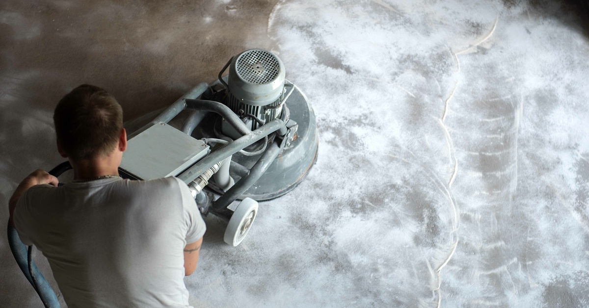 A professional floor finisher stands over a concrete polisher machine as they run the machine over the floors.