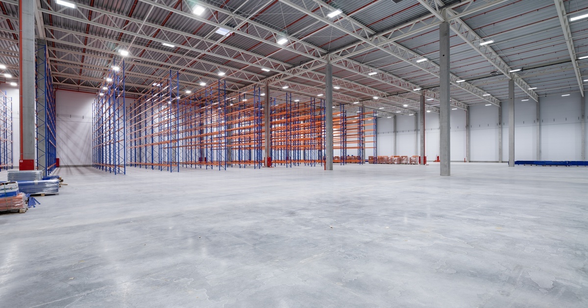 A large warehouse with concrete floors and rafters around the walls. The rafters are empty and there's nothing inside.