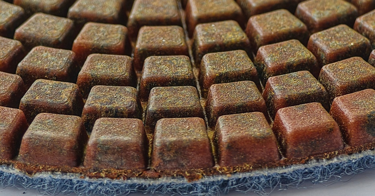 A close-up of a diamond polishing pad. The pad has small brown squares on the top and a felt surface on the bottom.