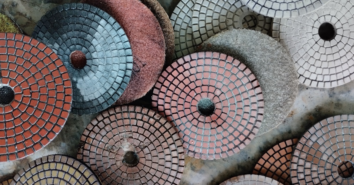 A pile of diamond polishing pads lays on a surface overlapping one another. Some are used and some are new.