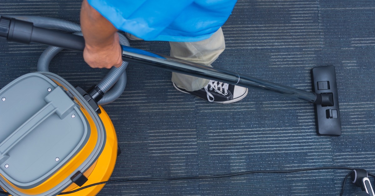 An aerial view of a professional cleaner walking down the carpeted halls of a commercial space with a vacuum.