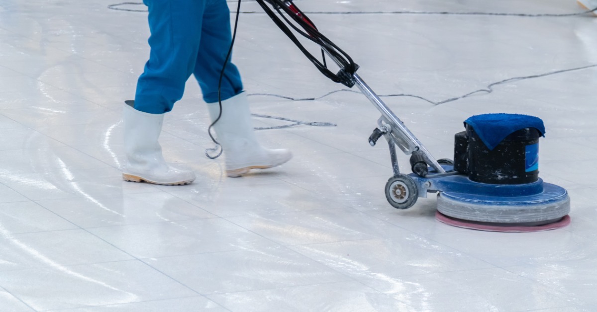 A floor care expert wears work pants and boots as they take a floor polishing tool to the large facility space.