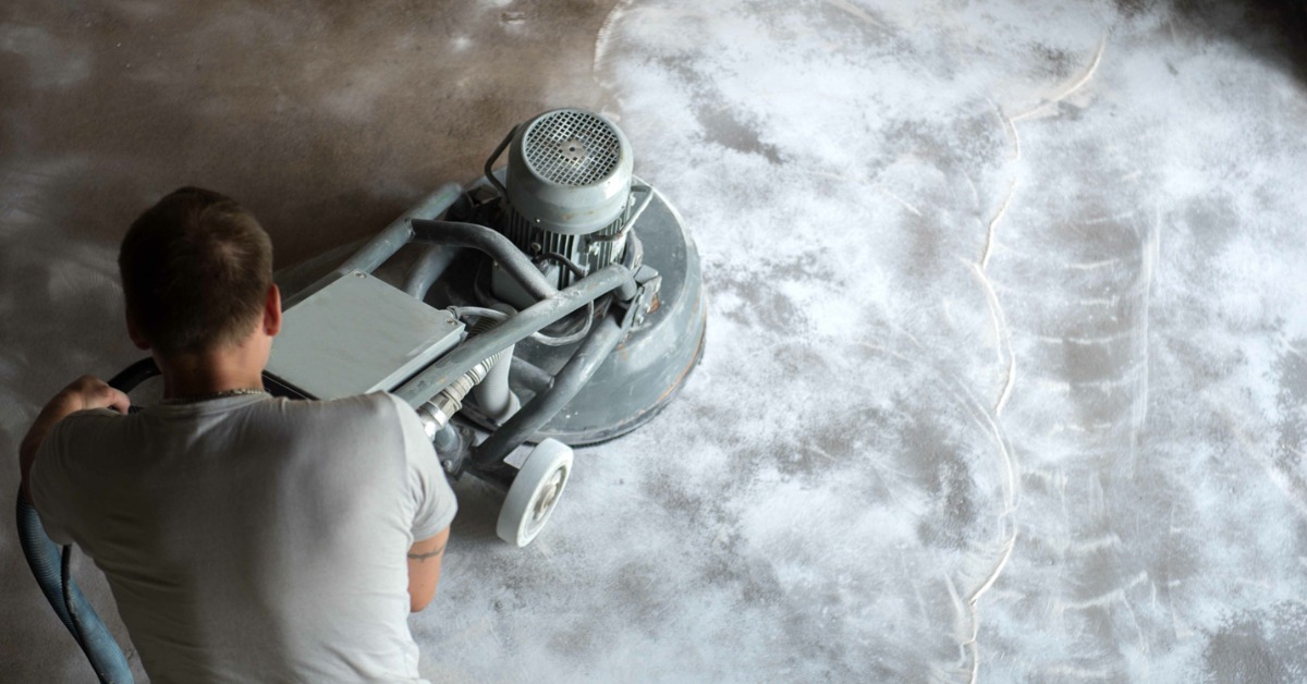 A professional floor cleaner waves a floor stripping machine across the flooring. The right side is sanded for new finish.