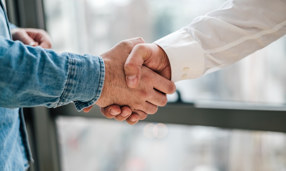 Business handshake between men. One is wearing a blue jean jacket, and the other is wearing a white shirt.