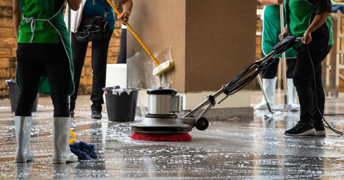 A group of janitors using different floor maintenance tools. Someone in the middle is using a floor buffer machine.