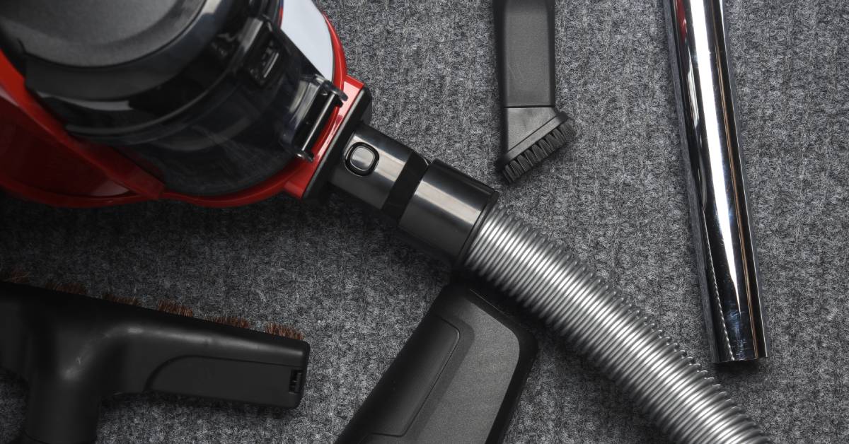 An industrial vacuum cleaner's attachments are on the ground. There’s a floor head, hose, bristle, and more.