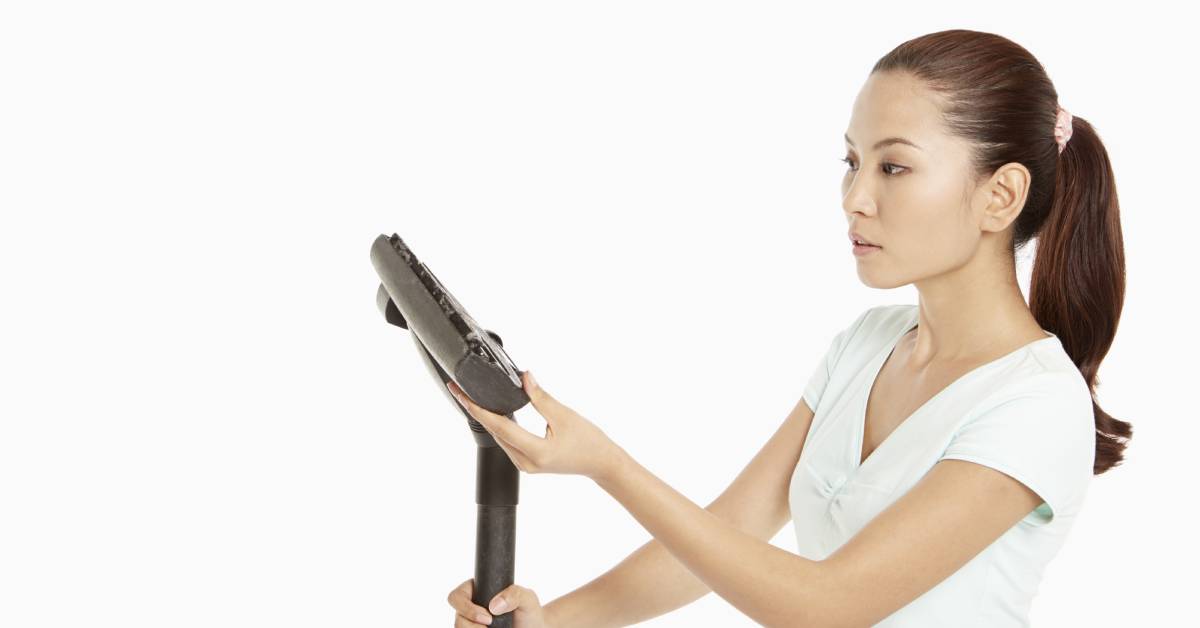A woman inspecting a vacuum cleaner nozzle to check for obstructions. She’s wearing a white shirt and has a ponytail.