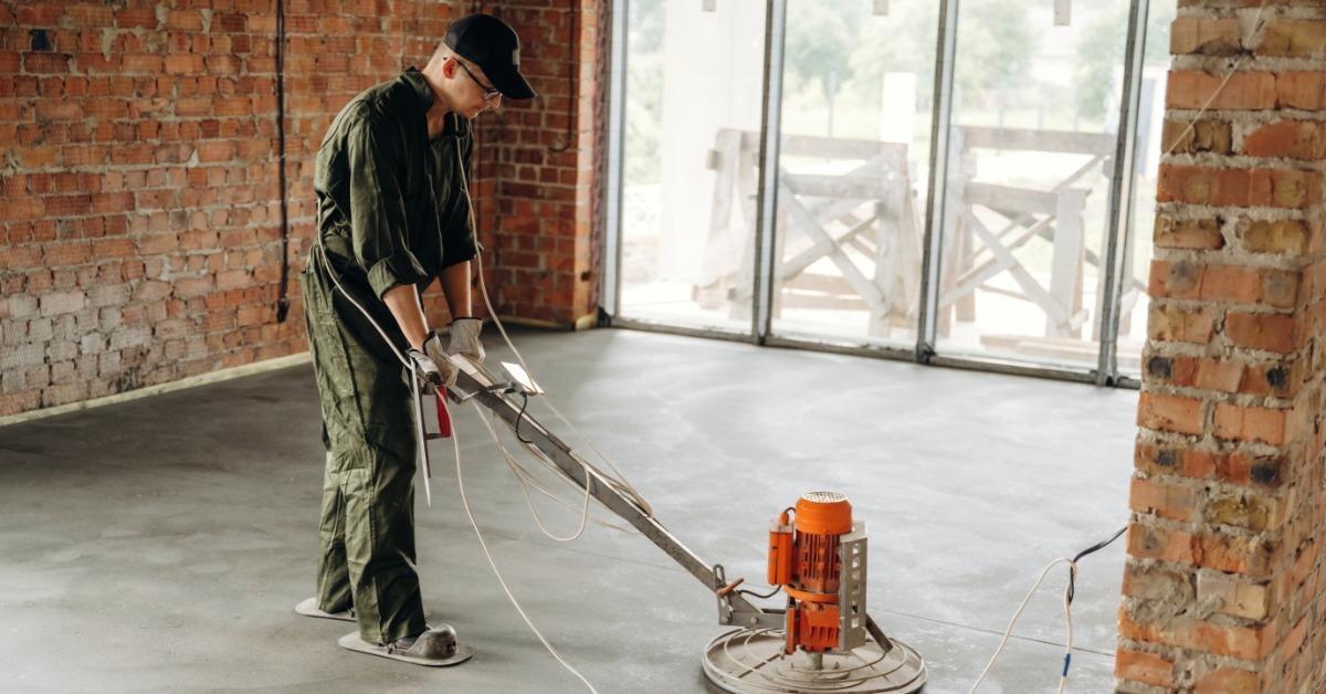 A professional flooring expert in uniform runs a concrete polisher machine across a room in a brick building.